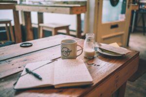 A table in a coffee shop with a journal, a pen, and a cup on top of it.