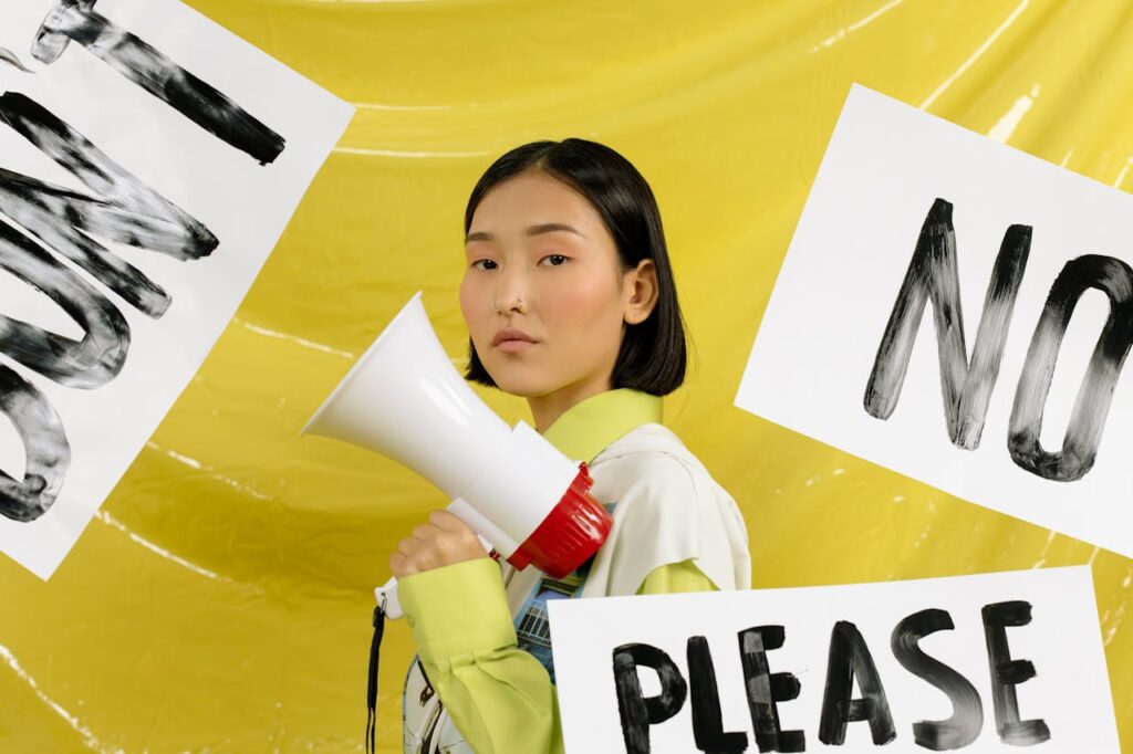 A woman holding a megaphone standing between signs saying “No” and “Please,” symbolizing setting boundaries.
