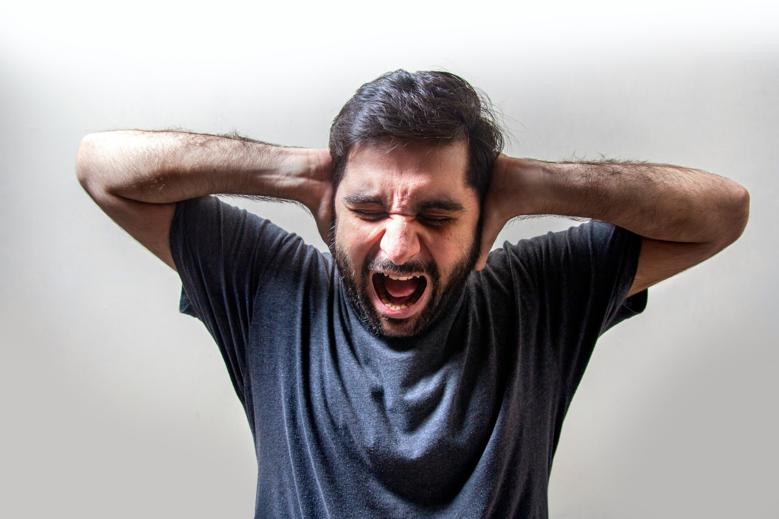 man yelling with eyes closed and hands over ears