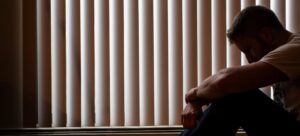 a depressed man sits against window blinds